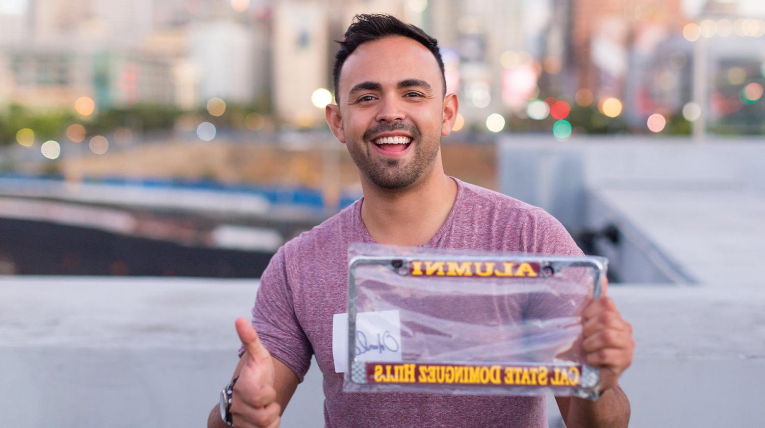 male alumn at a previous CSUDH alumni event holds CSUDH license plate gift